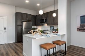 Saint Charles apartment for rent - Modern kitchen with designer lighting, dark cabinetry, stainless steel appliances and counter with seating  at Chapter at the Streets of St Charles, Saint Charles, 63303