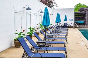 St. Charles apartment for rent - A poolside area with blue lounge chairs and umbrellas at French District Villas Apartments, Missouri