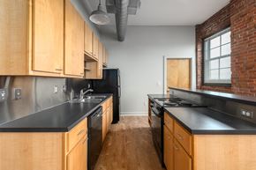 Saint Louis apartment for rent - a kitchen with wooden cabinets and black counter tops and a brick wall at Lofts at Lafayette Square Apartments, Saint Louis, MO, 63104
