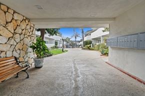 Redondo Beach apartment for rent - A stone wall and a wooden bench are on the left side of a concrete path.