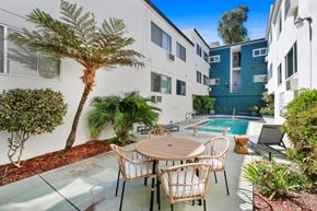 Hollywood apartment for rent - A patio with a table and chairs is surrounded by plants and a pool.