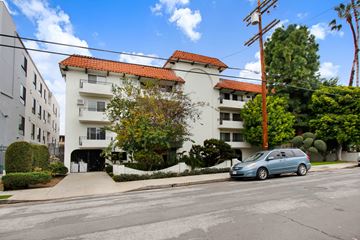 Los Angeles apartment for rent - A blue car is parked on the street in front of a white building with a red tile roof.