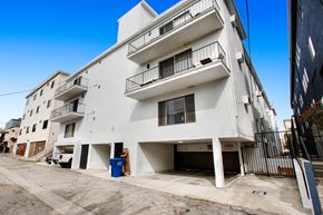 Los Angeles apartment for rent - A white building with balconies and a blue trash bin in front.