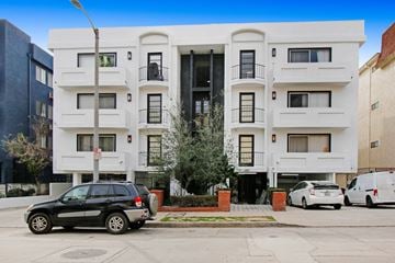 Los Angeles apartment for rent - A black SUV is parked in front of a white building with a tree in front of the building.