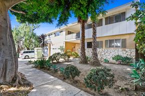Santa Monica apartment for rent - A white building with a balcony is surrounded by green plants and trees.