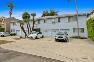 Los Angeles apartment for rent - A white car is parked in front of a grey building with a palm tree.
