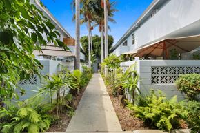 Los Angeles apartment for rent - A concrete walkway leads between two white buildings with a fence and green plants on either side.