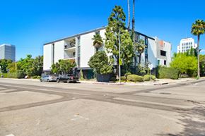 Los Angeles apartment for rent - A modern building with a white facade is surrounded by palm trees and other greenery.