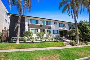 Los Angeles apartment for rent - A modern building with a white facade and balconies is surrounded by greenery and palm trees.
