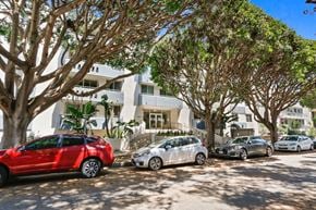 Santa Monica apartment for rent - A red car is parked in front of a white building with trees.