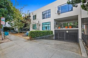 West Hollywood apartment for rent - A modern building with a black gate and a green bush in front.