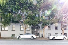 San Francisco apartment for rent - Two white cars are parked on the street in front of a building with trees.
