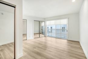 West Hollywood apartment for rent - A spacious room with wooden flooring and a view of a cityscape through the windows.