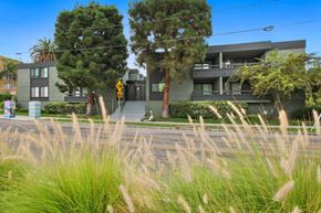 Los Angeles apartment for rent - A modern house with a grey exterior and a balcony is surrounded by tall grass and trees.