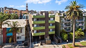 Los Angeles apartment for rent - A tall green and beige building with a palm tree in front.