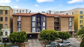 Los Angeles apartment for rent - A building with a red tile roof is in the middle of a street with cars parked in front.