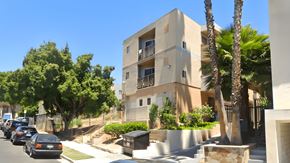 Los Angeles apartment for rent - A modern building with a balcony is surrounded by trees and parked cars.