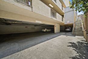 Los Angeles apartment for rent - A car is parked in a garage under a building with a staircase on the right side.