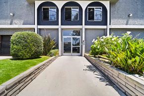 Hawthorne apartment for rent - A building with a grey facade and a white door is surrounded by greenery.