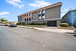 Hawthorne apartment for rent - A two-story building with a red tile roof and a garage door is situated on a street with cars parked on the side.