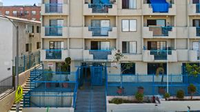 Los Angeles apartment for rent - A blue fence surrounds a building with a staircase leading to the entrance.