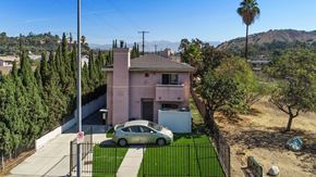 Los Angeles apartment for rent - A car is parked in front of a pink house with a black fence.