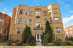 Chicago apartment for rent - A large brick building with a black iron fence in front.