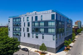 Chicago apartment for rent - A modern building with a flat roof and large windows is surrounded by a sidewalk and street.