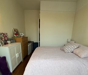 Chicago apartment for rent - A bedroom with a bed, nightstand, and a dresser with a clock and picture frame on top.