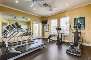 Kissimmee apartment for rent - A spacious home gym with treadmills, elliptical machines, and a fan.
