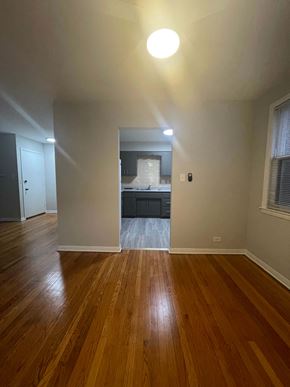 Chicago apartment for rent - A room with wooden floors and a kitchen visible through the door.