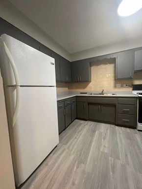 Chicago apartment for rent - A white refrigerator stands in a kitchen with grey cabinets and a wooden floor.