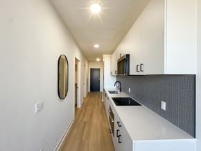 Chicago apartment for rent - A long, narrow kitchen with white cabinets and a black backsplash.