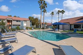 Avondale apartment for rent - Avondale, AZ, Affordable Apartments Near Goodyear Ballpark - The Peaks on 4th - A Swimming Pool With Lounge Chairs, Blue Umbrellas, Palm Trees, And Apartment Buildings.