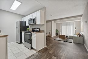 Aurora apartment for rent - Model Kitchen with White Cabinets and Tile Flooring with View of Living Room with Wood-Style Flooring at Liberty Creek Apartments in Aurora, CO.