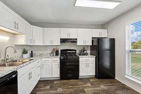 Kansas City apartment for rent - 3-Bedroom Apartments in Kansas City, MO - Parc at Creekside Apartments - Bright Kitchen With White Cabinets, Granite Look Counters, Black Appliances, Vinyl Plank Flooring, and Window Views.