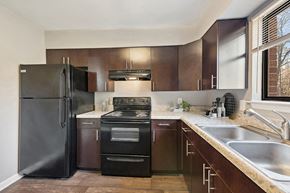 Raleigh apartment for rent - Pet-Friendly Apartments in Raleigh, NC - Spring Forest - U-Shaped Kitchen With Dark Wood Cabinets, Black Appliances, Double Sink, And Wide Countertops By Window Light.