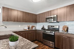 Sandy apartment for rent - Dog-Friendly Apartments in Sandy, UT - Seven Skies Apartments - Modern Kitchen With Granite Countertops, Stainless Steel Appliances, Subway Tile Backsplash, and Wood-Style Cabinets And Flooring.