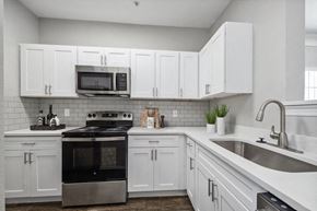 Lewisvillle apartment for rent - 3-Bedroom Apartments in Lewisville, TX - Bridges at Oakbend - Kitchen With White Cabinets, Tile Backsplash, Stainless-Steel Appliances, Range With Microwave, And Double Sink With Sleek Faucet.