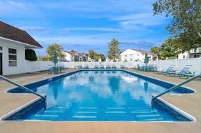 Marshfield apartment for rent - Apartments for rent in Marshfield, MA - Village At Marshfield - Resort-Style Outdoor Pool With Blue Water, Entry Handrails, Lounge Chairs, And Umbrellas Inside White Fenced Courtyard.