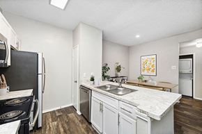 Dallas apartment for rent - Model Kitchen with White Cabinets and Wood-Style Flooring with View of Dining Room at Dallas North Park Apartments in Dallas, TX.