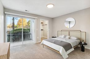 Jonesboro apartment for rent - 3-Bedroom Luxury Apartments in Jonesboro, GA - The Park at Tara Lake - A Bedroom With Large Sliding Glass Door, Neutral Carpet, Modern Bed With Side Tables, And Round Wall Mirror.
