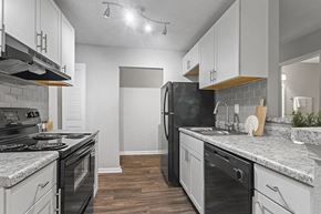 Peachtree Corners apartment for rent - 2-Bedroom Affordable Apartments in Peachtree Corners, GA - Corners At 1700 - Kitchen With White Cabinets, Tile Backsplash, Black Appliances, Track Lighting, And Hardwood-Inspired Floors.