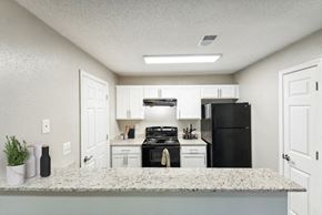 Charlotte apartment for rent - 2-Bedroom Affordable Apartments in East Charlotte, NC - Woodland Estates - A Kitchen With White Cabinets, A Breakfast Bar, A Black Refrigerator, And A Stove.