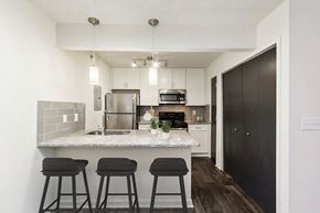 Marietta apartment for rent - Marietta, GA, Luxury Apartments for Rent - The Grandstand - A Kitchen With White Cabinets, Stainless Steel Appliances, Quartz Breakfast Bar With Three Stools, And Pendant Lights.