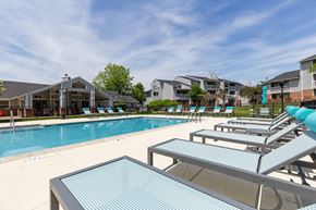 Aurora apartment for rent - Community pool with sun loungers and a table in the foreground with apartment buildings in the background.