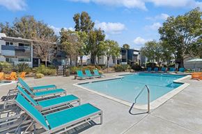 El Cajon apartment for rent - Apartments in El Cajon, CA - Colonnade at Fletcher Hills - Resort-Style Swimming Pool with Turquoise Lounge Chairs, Pool Steps and Handrail, Spacious Deck, and Apartment Buildings Under Blue Sky.
