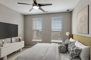 Marietta apartment for rent - 2-Bedroom Luxury Apartments in Marietta, GA - Parkside at Town Center - Modern Bedroom With Upholstered Headboard, Ceiling Fan, Dual Windows With Blinds, And Wall-Mounted Television On Dresser.