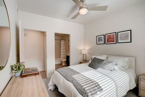 West Valley City apartment for rent - West Valley City, UT, Pet-Friendly Apartments - Sage Valley - A Bedroom With A White Bed, Ceiling Fan, Nightstand Lamp, Framed Wall Art.