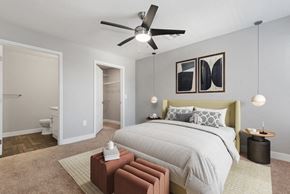 Surprise apartment for rent - Three-Bedroom Modern Apartments in Surprise, AZ - Harmony at Surprise - A Bedroom With A Large Bed With Neutral Bedding, Ceiling Fan, Pendant Lights, And Abstract Wall Art.